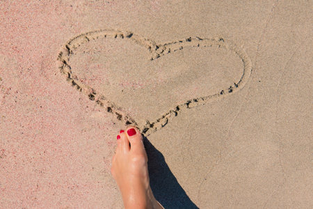 Girl drawing a heart in the pink sand with her foot. Holiday and relax concept.の写真素材
