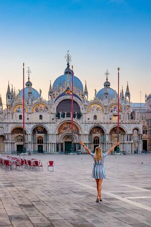 Woman enjoying the view of San Marco Cathedral in Venice, Italy. A slender woman with her hands up. Sunrise on St. Mark's square.の写真素材
