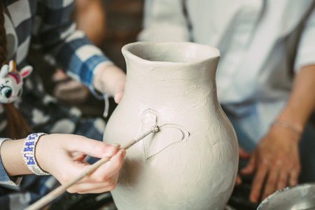 Girl's hands draw a heart on a ceramic vase on a potter's wheelの写真素材