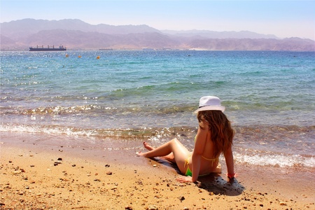 young girl with long hair in the bikini and a white hat on the beachの写真素材