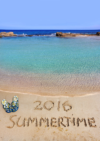 inscription summertime 2016 on the wet sand of the sea beach in a quiet cove of the Mediterranean Sea and beach slippersの写真素材