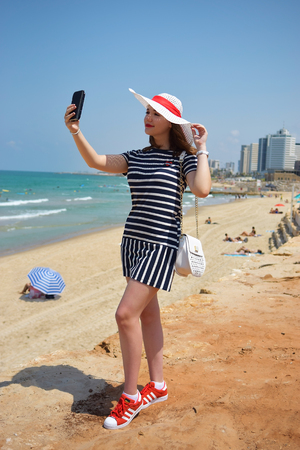 young woman taking a selfie against the background of modern luxury hotels and beach of Tel Aviv - Jaffa, Israelの写真素材
