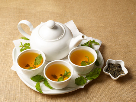 Green tea - hot green tea in a kettle and cups with immersed mint leaves on a jute backgroundの写真素材