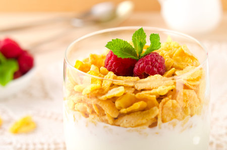 Breakfast with cereal flakes, yogurt and fresh raspberries served in glass
