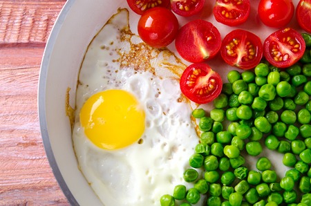 Breakfast with fried egg, green peas and cherry tomatoes in red panの写真素材