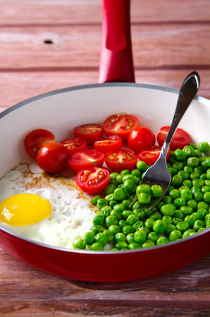 Breakfast with fried egg, green peas and cherry tomatoes in red panの写真素材