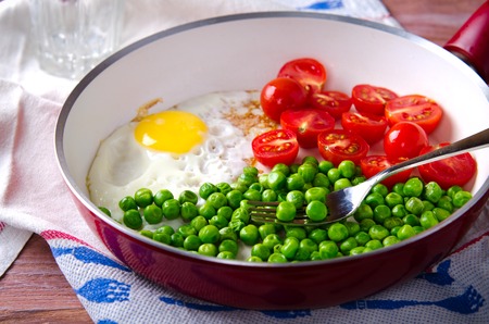 Breakfast with fried egg, green peas and cherry tomatoes in red panの写真素材