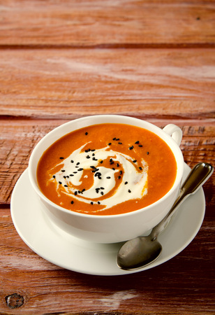 Pumpkin Soup with tomatoes, chili, yogurt and black sesame seeds on wooden backgroundの写真素材