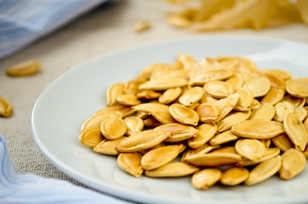 Baked and Salted Pumpkin Seeds on white plateの写真素材