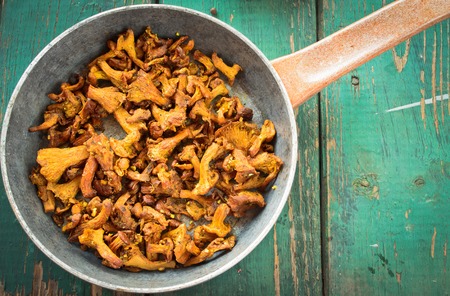 Fried Chanterelles with onions and fresh herbs in skillet on wooden backgroundの写真素材
