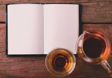 Open blank notepad on old wooden table with black teaの写真素材