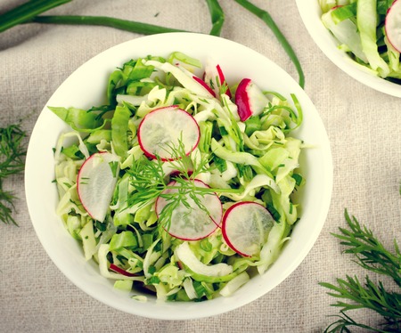 Fresh vegetables salad with cabbage, radishes. dill and greens on white bowlの写真素材