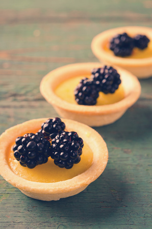 Homemade round tartlets with lemon curd and fresh blackberries on wooden tableの写真素材
