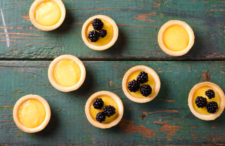 Homemade round tartlets with lemon curd and fresh blackberries on wooden table