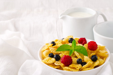 Breakfast with cereal flakes, berries, mint and milk, on white background
