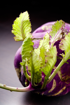 Purple kohlrabi cabbage with green leaves on dark wooden tableの写真素材