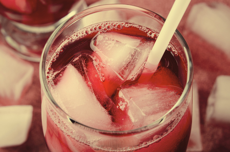Cold cherry drink with ice cubes and cocktail tubes in glasses, on pink backgroundの写真素材