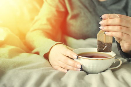 Female hands holding a cup of hot tea on warm blanket.の写真素材