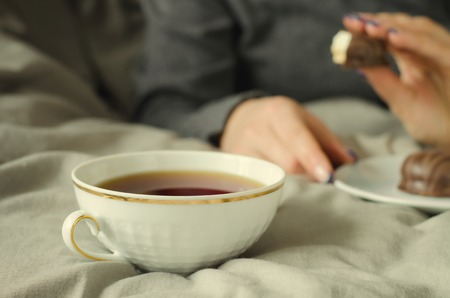 Female hands holding a cup of hot tea on warm blanket.の写真素材