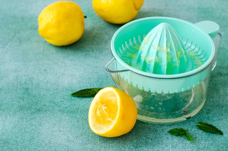 Fresh lemons and mint with citrus squeezer on turquoise background. Copy spaceの写真素材