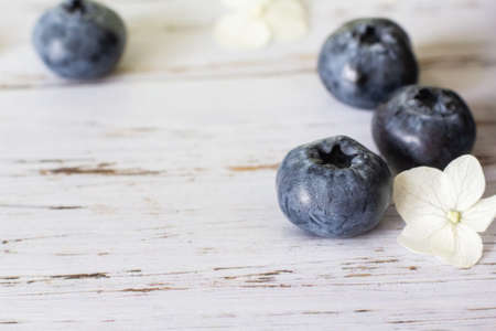 Ripe blueberries, hydrangea flowers nearby. Light wooden backgroundの写真素材