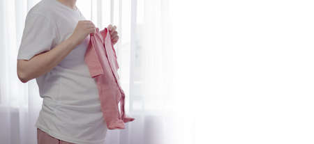Pregnant woman holding baby clothing. Birth preparation conceptの写真素材