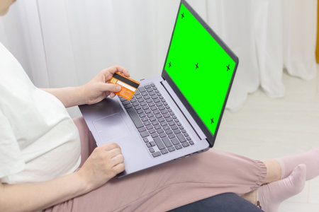 Green screen design concept. Side view of woman hands holding credit card using laptop at home, data...