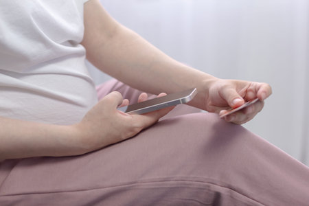 Pregnant girl holds a credit card in her hands and looks at the phone with a green screen.