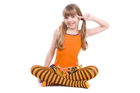 Little girl in the orange dress with finger near her head is sitting on the floor. Portrait of an attractive young teenager is  playing the fool and smiling in orange over white background.の写真素材