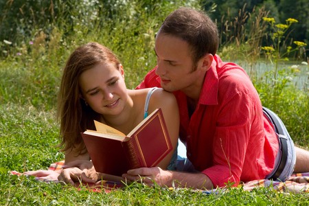Young cople laying on a blanket on the grass on a hot summer day and reading book.  Woman and man are enjoying the sunshine in a park. Just happy couple relaxing.の写真素材