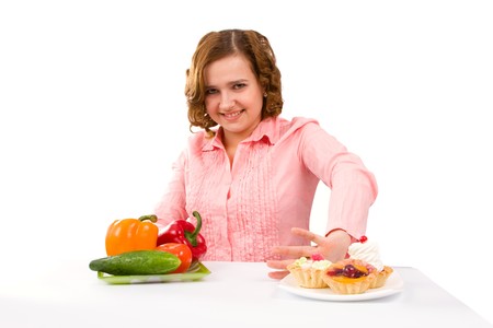 Woman makes choice between cakes and healthy vegetables on white background.  To eat or not to eatの写真素材