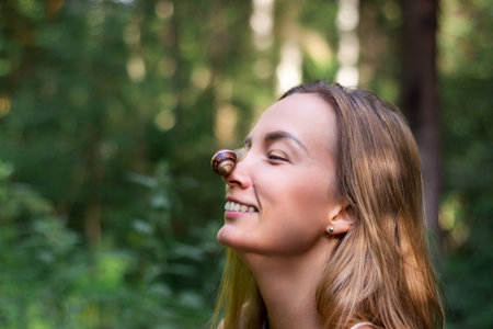 Snail sits on nose of woman. Girl laughs and looks at clam. Close-up portraitの写真素材