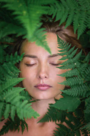 Portrait of a Caucasian woman in large green fern leaves. Close-up in the grassの写真素材