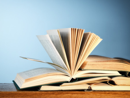 Close-up of a pile of old open novel books on a wooden table, with copy space on blueの写真素材