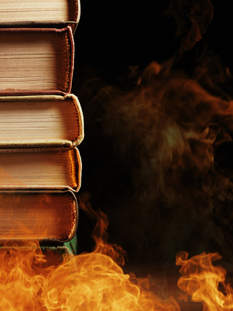 Pile of hardcover books surrounded with swirling tendrils smoke or vapor in a darkened vintage style room conceptual of magic, fire, spirituality or alchemyの写真素材