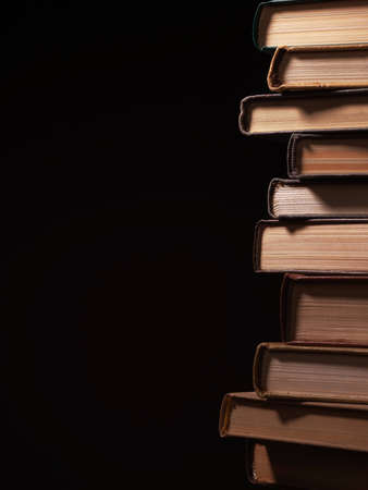 Pile of hardcover books stacked on top of one another in a shadowy room on a wooden desk with copyspace in the foregroundの写真素材