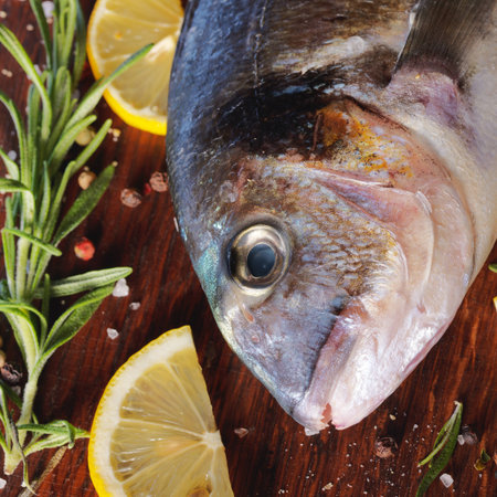 Raw dorado fish with rosemary and sea salt server on old wooden table.