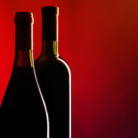 Bottles of red wine on dark red background. Filtered image: vintage effect.の写真素材