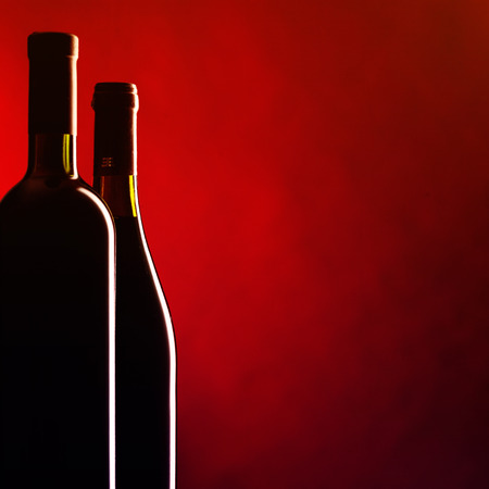 Bottle and glass of red wine on dark red background. Filtered image: vintage effect.の写真素材