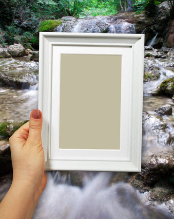 Wooden frame in beautiful woman hands. Waterfall on the background
