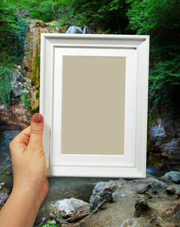 Wooden frame in beautiful woman hands on the background of natural spring waterfall