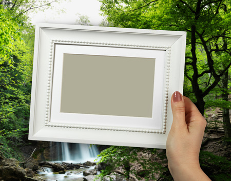 Wooden frame in beautiful woman hands. background of the Natural Spring Waterfallの写真素材