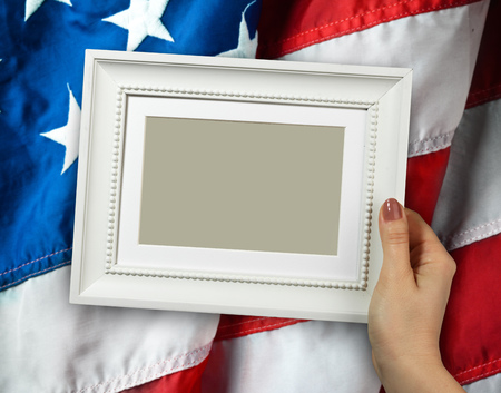 Wooden frame in beautiful woman hands on the background of flapping flag USA with waveの写真素材