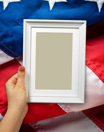 Wooden frame in beautiful woman hands on the background of flapping flag USA with waveの写真素材