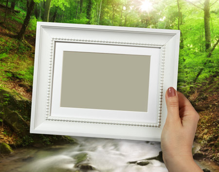 Wooden frame in beautiful woman hands on the background creek in the forest