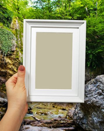 Wooden frame in beautiful woman hands on the background waterfall in forestの写真素材