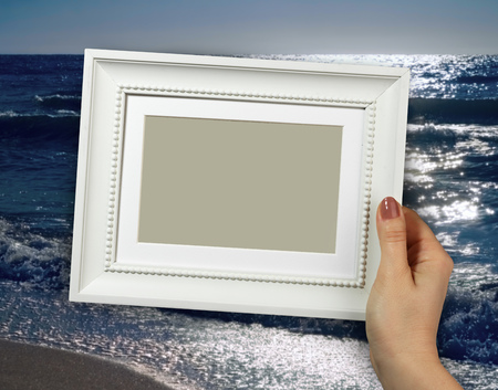 Wooden frame in beautiful woman hands on the background sea waves on beaches, sands, foamの写真素材
