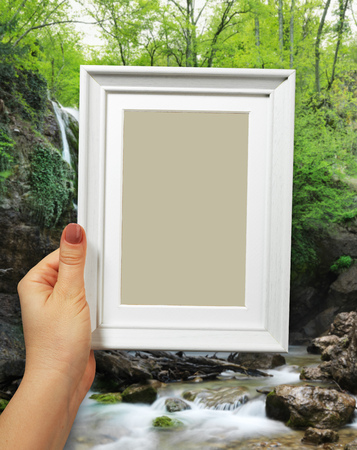 Wooden frame in beautiful woman hands. Waterfall on the backgroundの写真素材