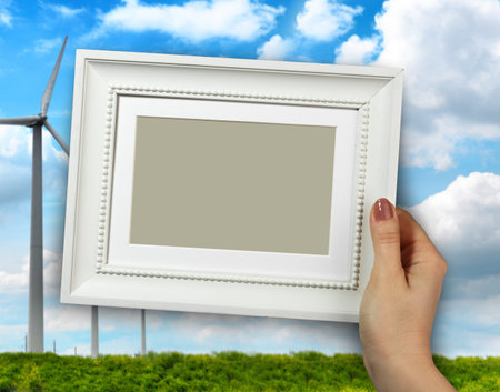 Wooden frame in beautiful woman hands. wind mill turbine in a farmland on the background