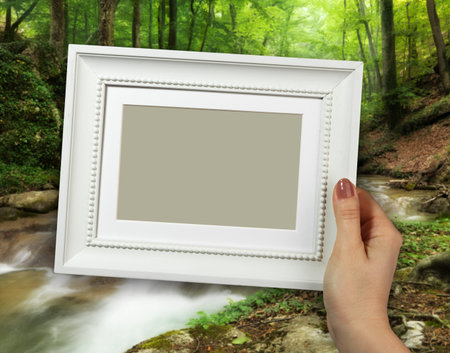 Wooden frame in beautiful woman hands on the background creek in the forest
